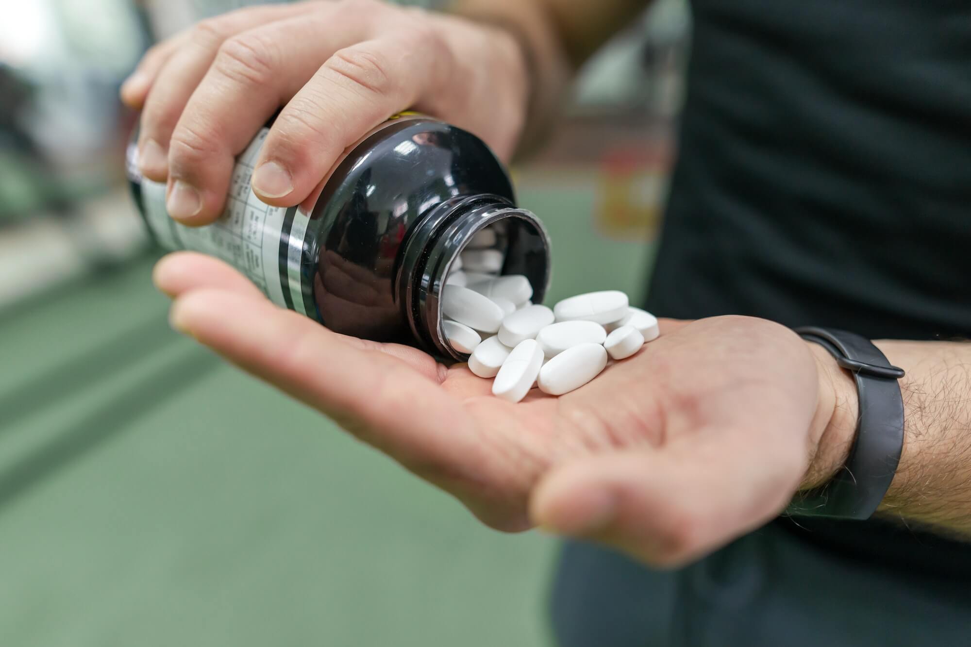 Closeup of sporty muscular man arms showing sports and fitness supplements, capsules, pills